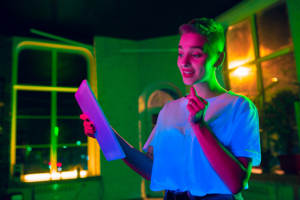 delightful-cinematic-portrait-stylish-woman-neon-lighted-interior-toned-like-cinema-effects-bright-neoned-colors-caucasian-model-using-tablet-colorful-lights-indoors-youth-culture